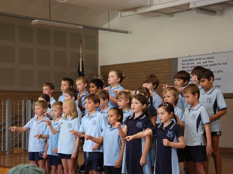 A class of students performing sign language in te hall during an assembly.