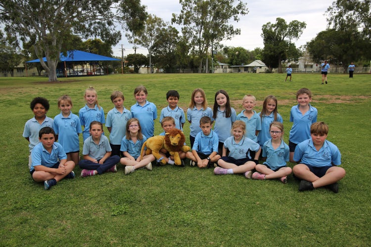 Year 2 Pandas sitting, with our Attendance award mascot in the playground. Students playing in the background.