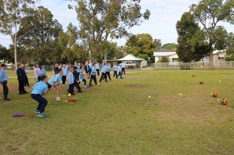 Students standing in a line throwing tennis balls at soccer ball in a traditional indigenous game games