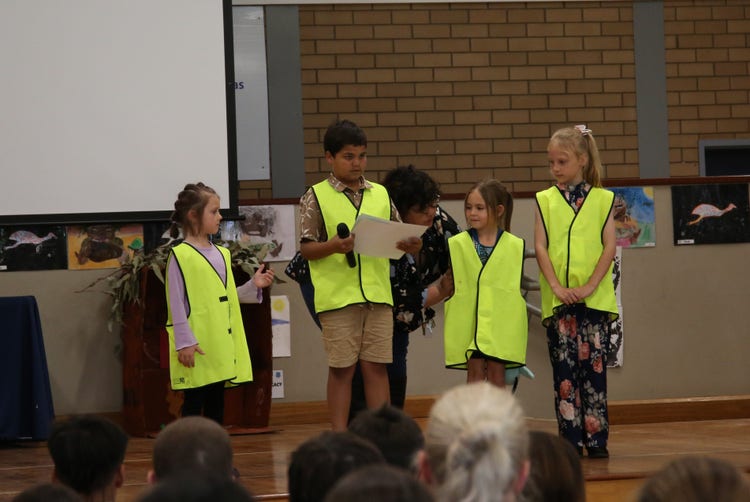 4 students leading the presentation of certificates during assembly on stage