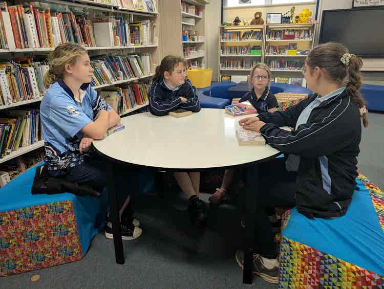 4 students sitting at a round table talking about the books they are reading