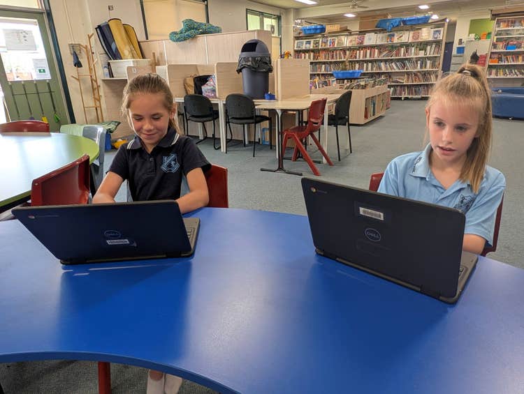2 students working on chromebooks in the library